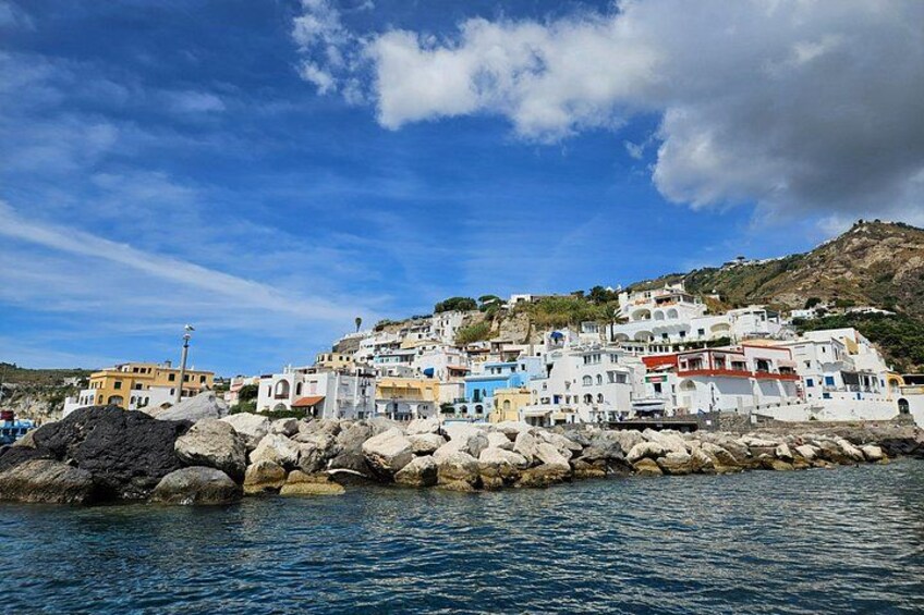 A coastal village with white buildings, rocky shoreline, and clear blue sky. 2