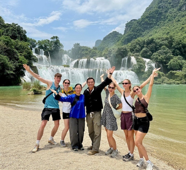 A group of people posing in front of a waterfall with lush greenery in the background. 1