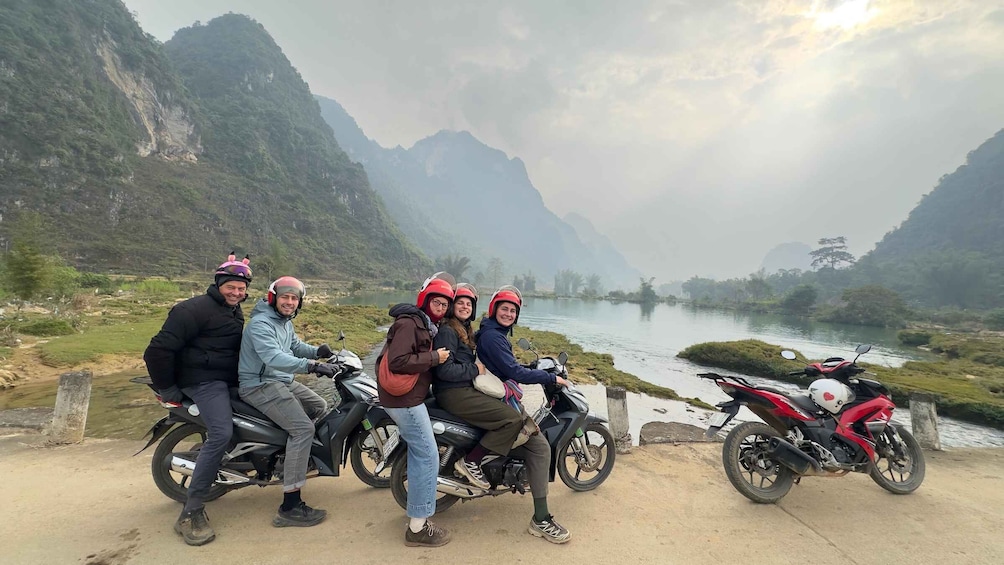 A group of people on motorcycles by a river with mountains in the background. 3