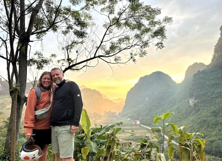Two people standing by a tree with a mountainous landscape in the background. 5