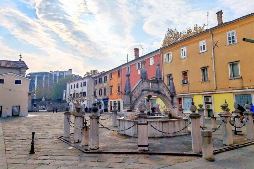 A historic square with a fountain, colorful buildings, and cobblestone pavement. 2