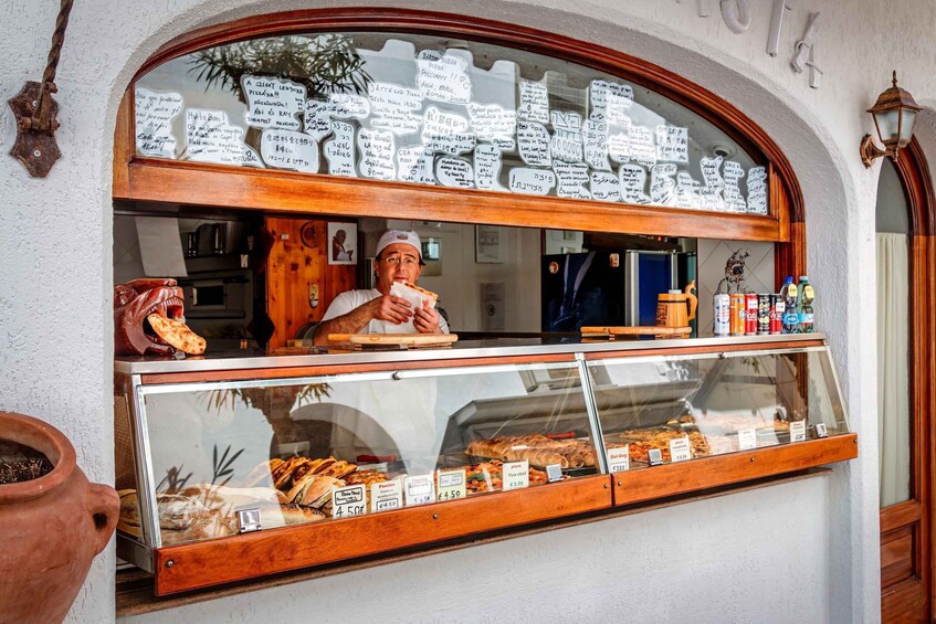 A bakery with a display case of baked goods and handwritten notes on the window. 5