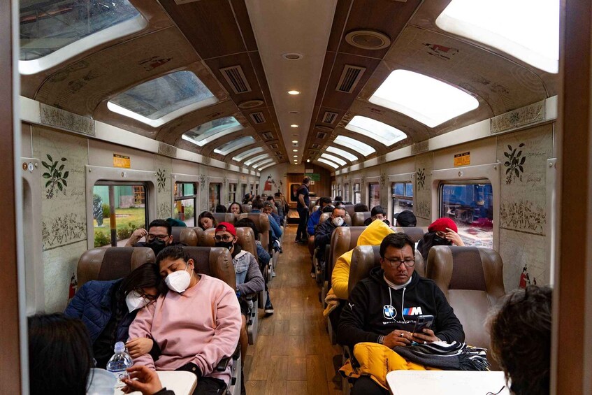 A train interior with passengers seated, some using their phones, and others resting. 5