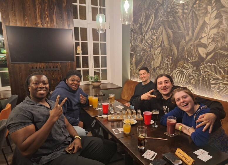 A group of people sitting around a table with drinks and playing cards. 5