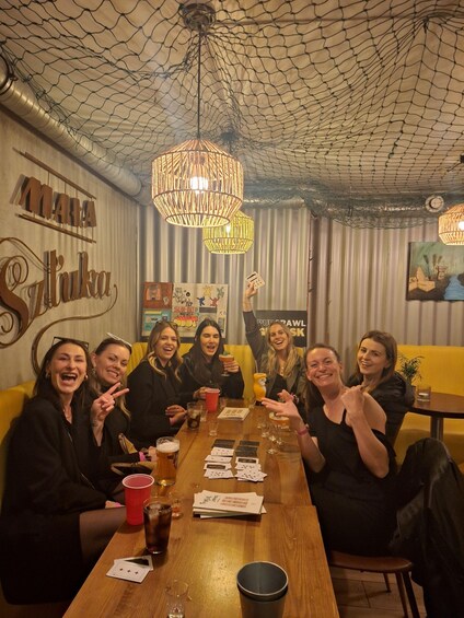 A group of people sitting around a wooden table in a restaurant with a netted ceiling and hanging lamps. 1