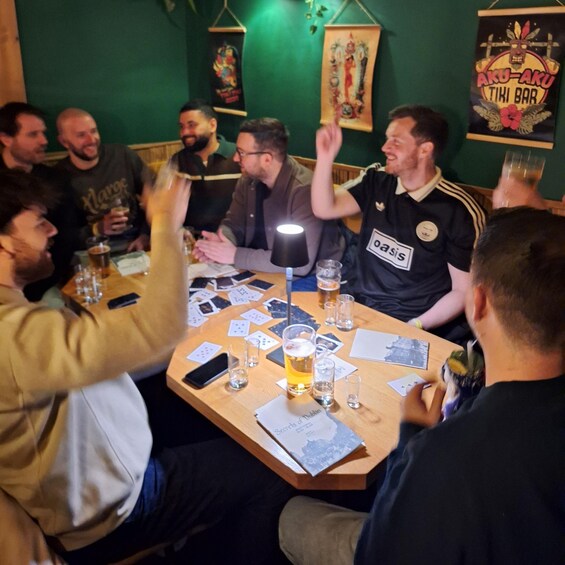 A group of people playing cards at a table with drinks and cards scattered around. 3