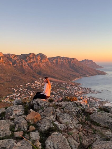 A person sitting on a rocky outcrop overlooking a coastal town and cliffs. 1