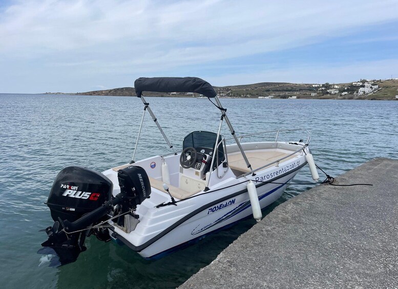 A white motorboat with a black canopy, docked at a pier with a calm sea and a hilly coastline in the background. 3