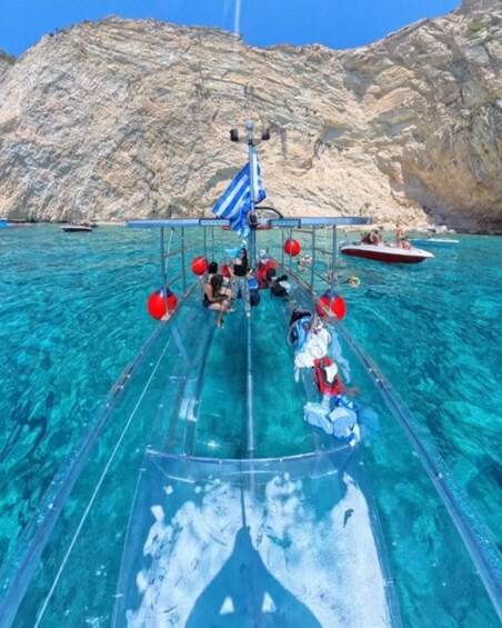 A clear blue boat with passengers and a flag, sailing near rocky cliffs. 3