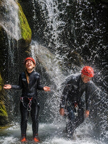 Two people in wetsuits and helmets near a waterfall. 4