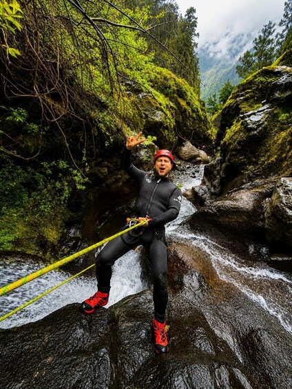 A person rappelling down a rocky waterfall in a forested area. 2
