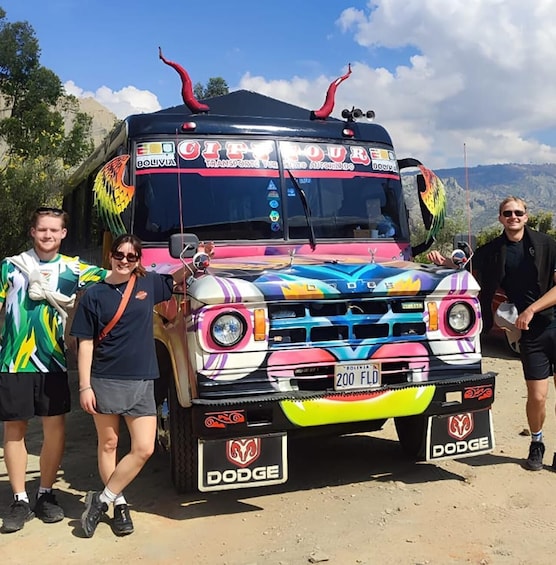 A colorful bus with 'City Tour Bolivia' and 'Dodge' branding parked on a dirt road with mountains in the background. 1