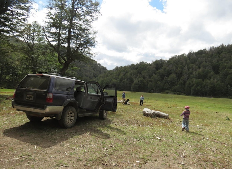 A black SUV parked in a grassy field with its door open, surrounded by trees and a few people. 2