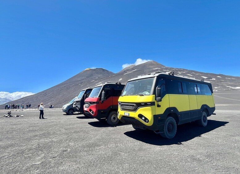 A yellow and red van parked on a gravel surface with a mountainous background and a clear blue sky. 2