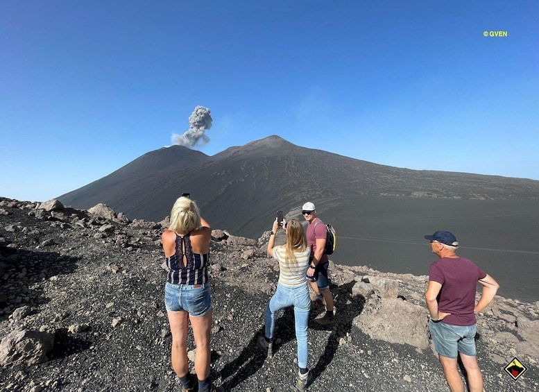 A group of people observing a volcano with smoke and ash plumes. 5