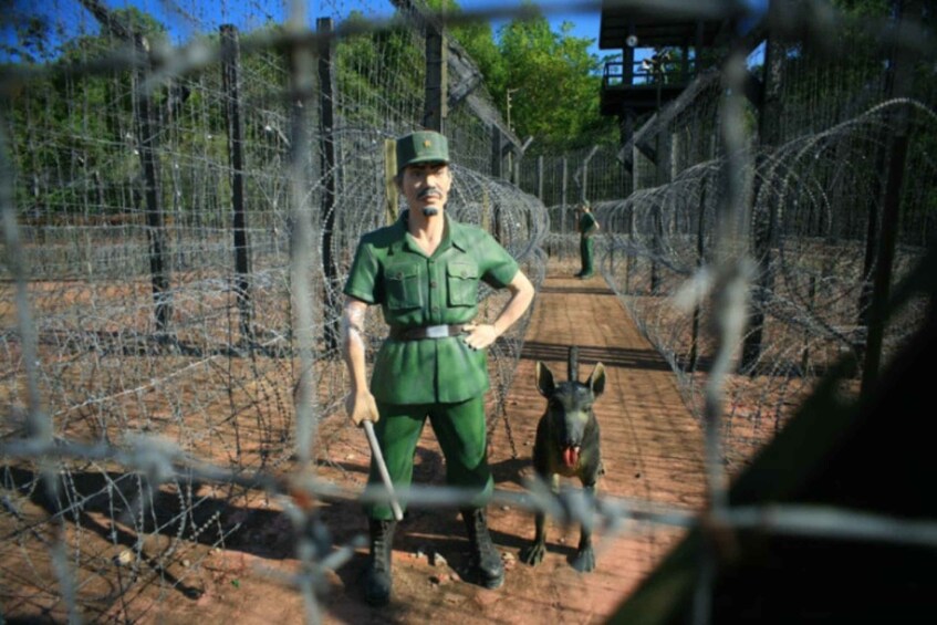 A person in military uniform standing behind barbed wire with a dog. 4