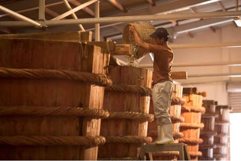 A person handling a large bundle of rope in a warehouse with wooden barrels. 2