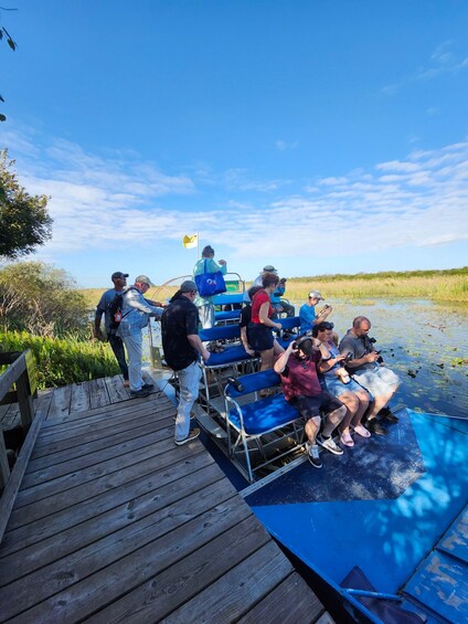 A group of people on a boat docked at a wooden pier with a marshy landscape in the background. 3