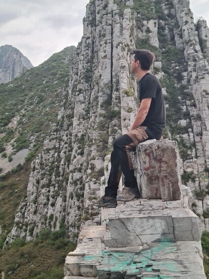 A person sitting on a rock ledge with a mountainous landscape in the background. 4
