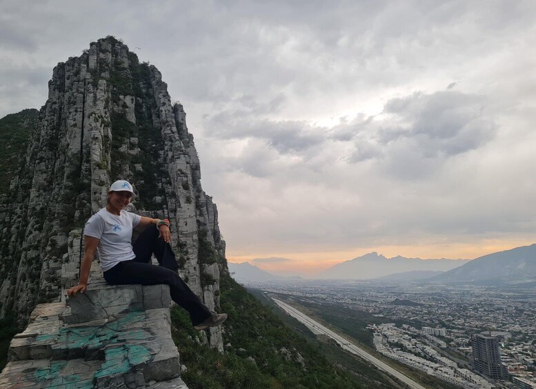 A person sitting on a stone ledge with a cityscape and mountains in the background. 5