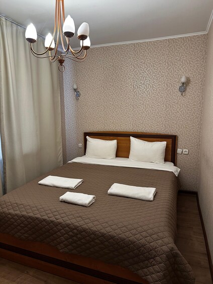 A neatly made bed with a brown quilt, white pillows, and folded towels. 4
