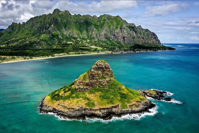 A mountainous island with a prominent peak, surrounded by turquoise waters and a sandy beach. 1