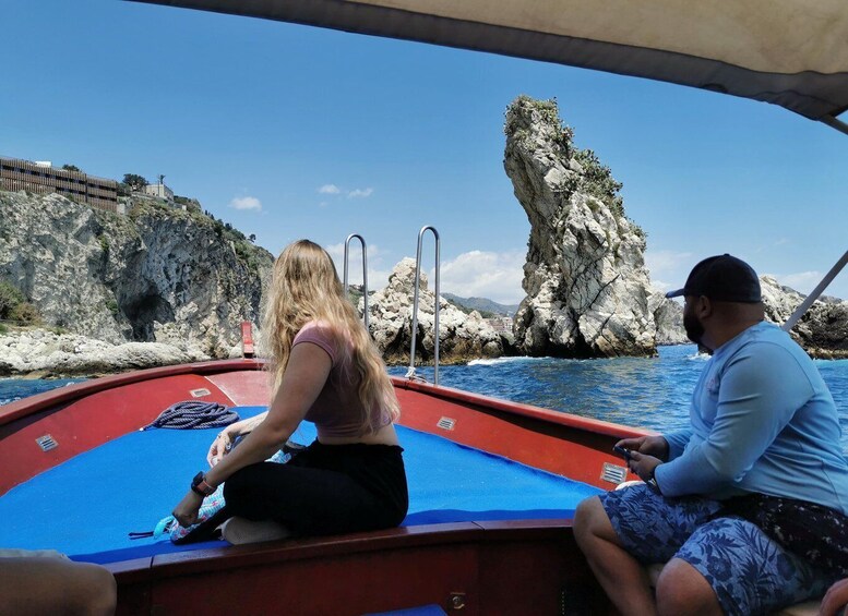 Two people on a boat with a rocky coastline and a prominent rock formation in the background. 1