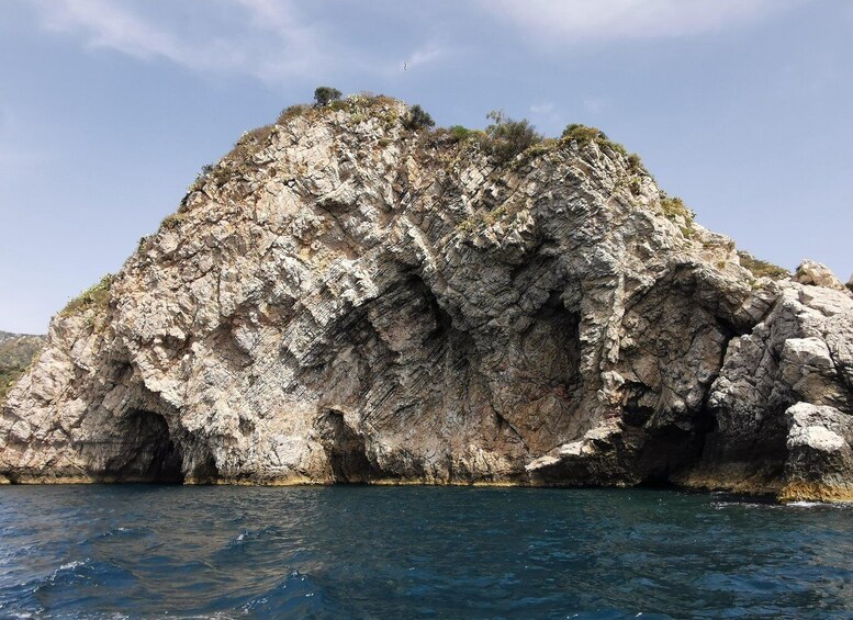 A rocky coastal formation with a clear blue sea in the foreground. 3