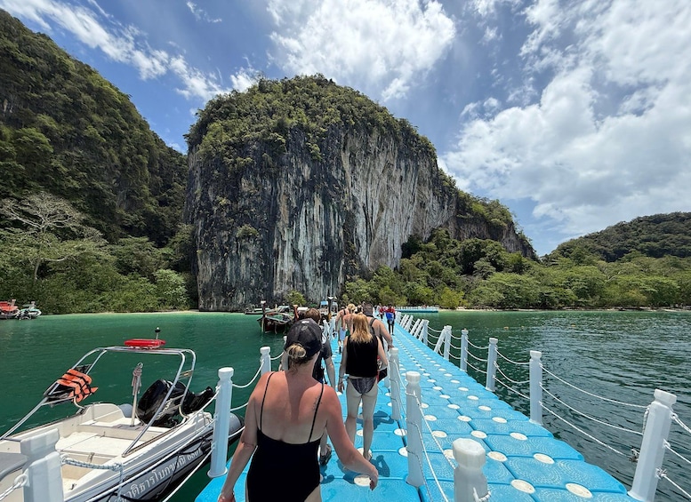 A pier leading to a boat, surrounded by lush green hills and a large cliff. 3