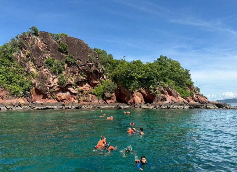 A group of people snorkeling in clear blue water near a rocky coastline with lush greenery. 4