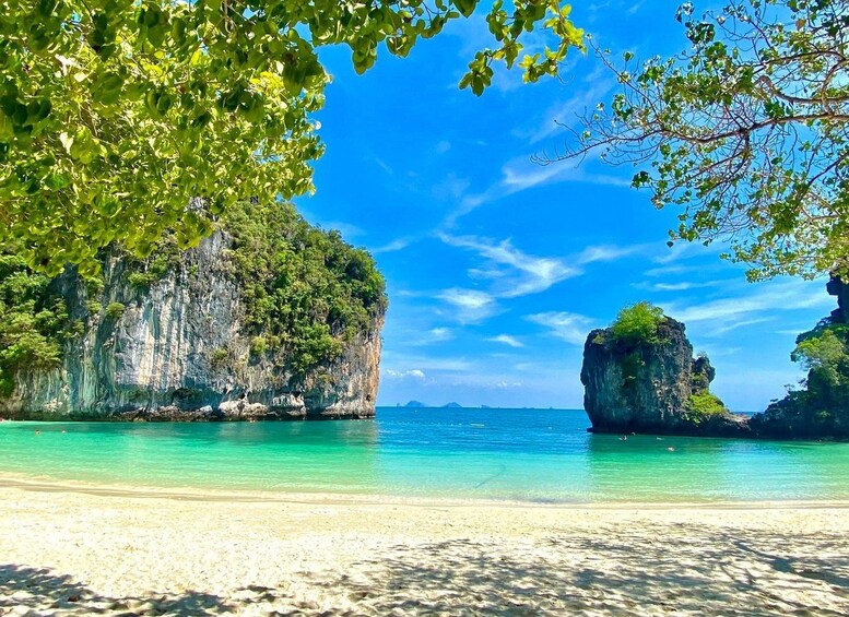 A beach with clear turquoise water, a sandy shore, and two prominent rock formations surrounded by lush greenery. 1