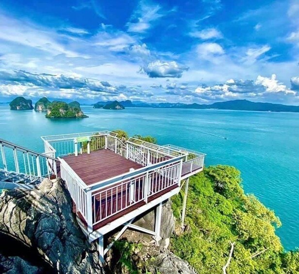 A wooden viewing platform with a railing overlooking turquoise waters and green islands. 4