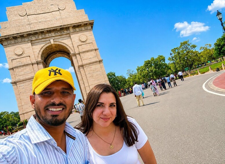 A couple taking a selfie in front of a large archway with the word 'INDIA' visible on it. 2