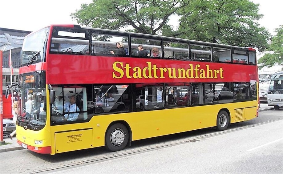 A yellow and red double-decker bus with the text "Stadtrundfahrt" on the side, parked on a street. 5