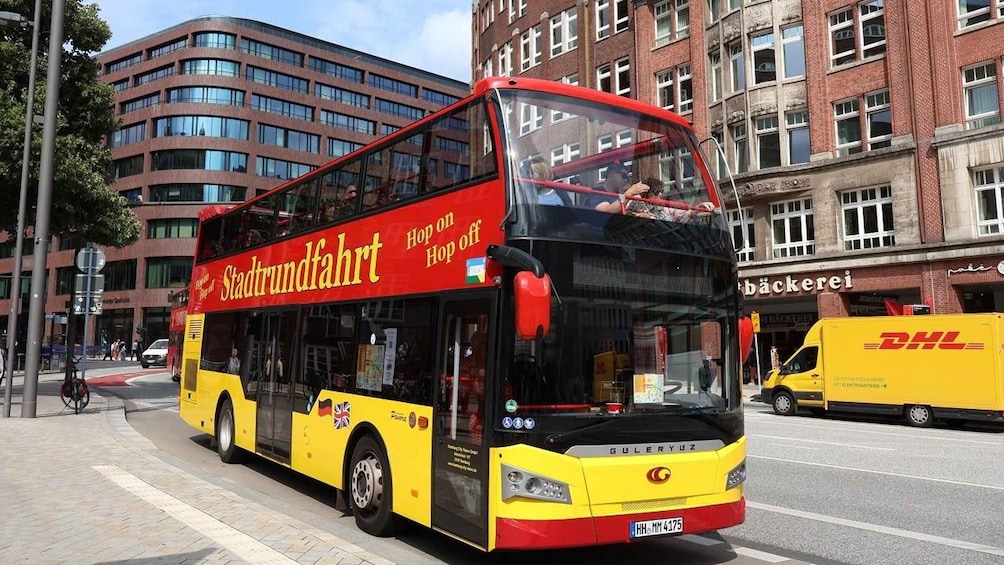 A yellow and red double-decker bus with 'Stadtrundfahrt' written on the side, driving on a city street. 1