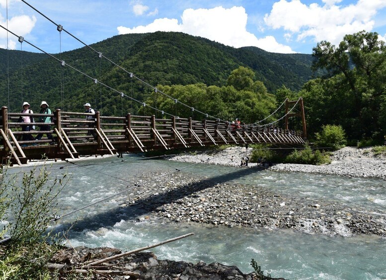 A suspension bridge over a river with people crossing, surrounded by a mountainous landscape. 5