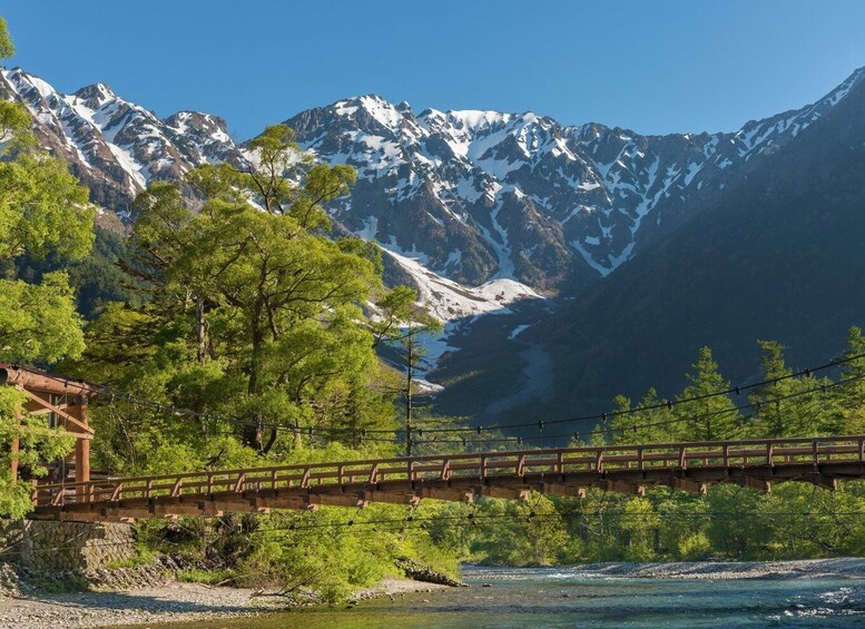 A wooden bridge over a river with snow-capped mountains in the background. 2