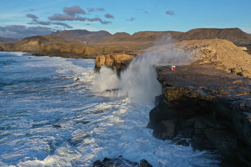 A coastal landscape with a rocky cliff and waves crashing against it. 3