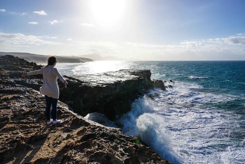 A person standing on a rocky cliff overlooking the ocean with waves crashing against the rocks. 4
