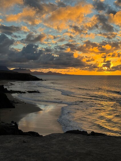 A beach at sunset with waves, a rocky shoreline, and distant mountains. 5