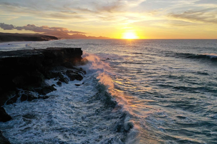 A sunset over the ocean with waves crashing against a rocky shore. 1