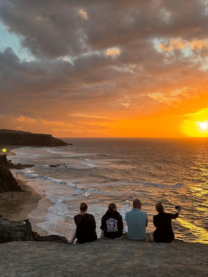 Four people sitting on a beach, watching the sunset over the ocean. 2