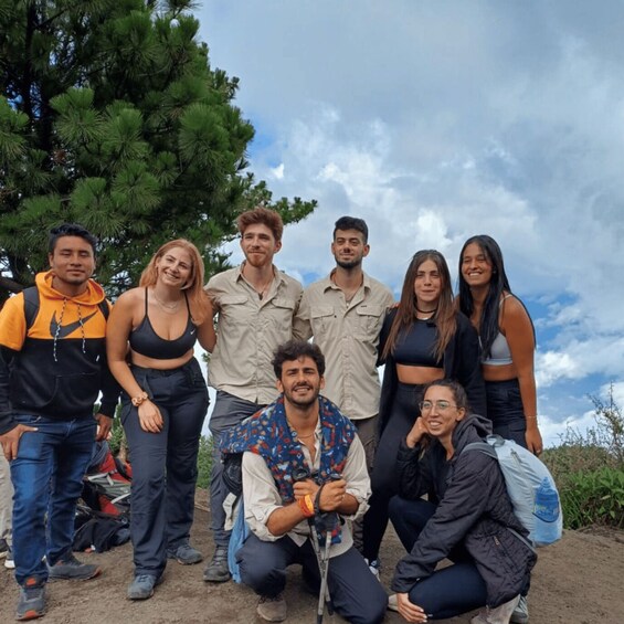 A group of people outdoors, some standing and some kneeling, with trees and a cloudy sky in the background. 2
