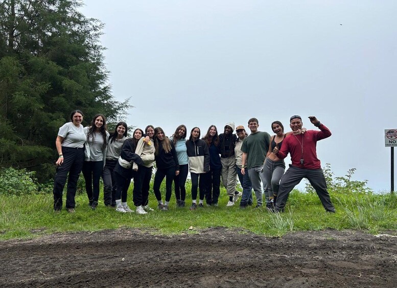 A group of people standing on a grassy field with a dirt path in the foreground and a sign in the background. 1