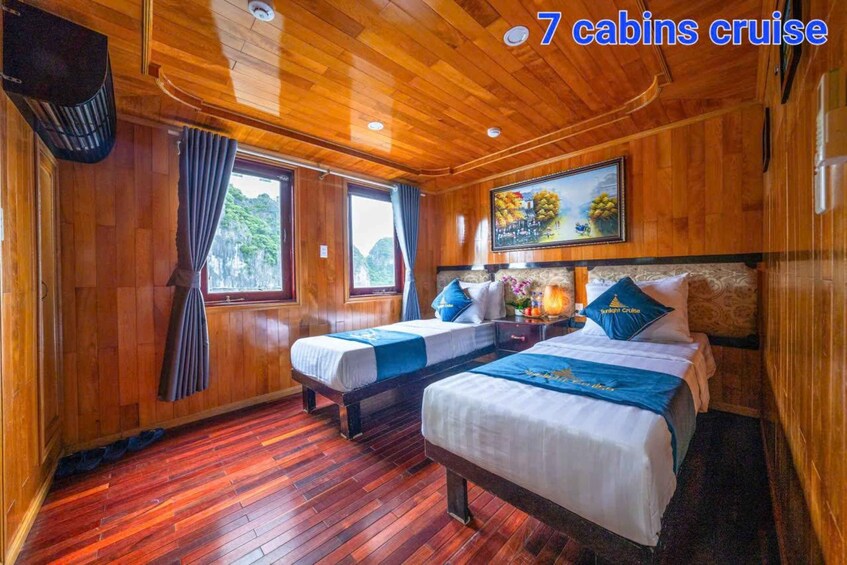 A cabin with wooden walls and floors, two beds, a painting, and a window with curtains. 2