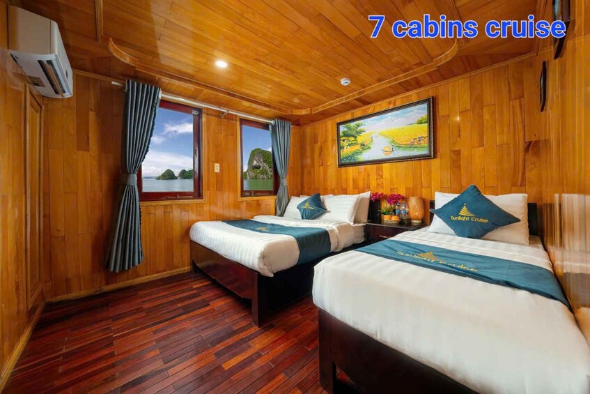 A cabin with wooden walls and floors, two beds with matching bedding, a painting, and a window with a view of the sea. 4