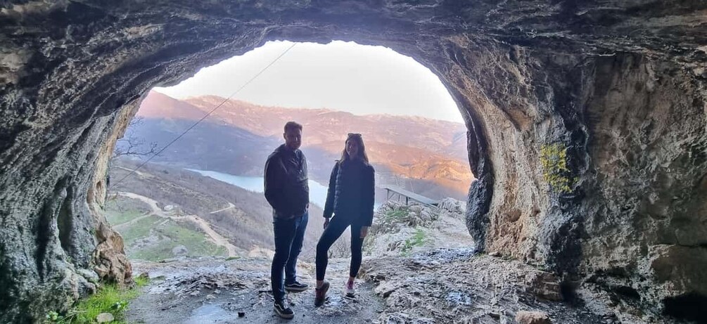 Two people standing in a cave with a view of a valley and mountains. 5