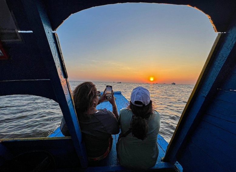 Two people on a boat during sunset, one taking a photo. 5