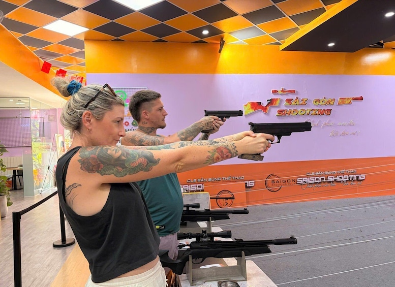 Two individuals aiming at a shooting range with firearms, surrounded by a vibrant orange and purple wall with text. 5