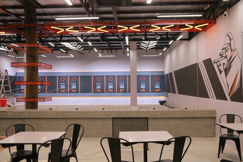 Un campo de tiro cubierto con objetivos numerados, mesas, sillas y un mural en la pared. 3